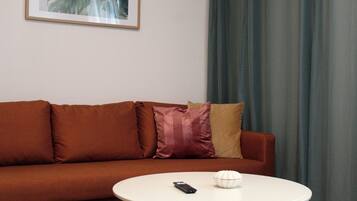 Ein Zimmer mit einem braunen Sofa, einem weißen Tisch, einer Fernbedienung und einem weißen Dekorationsobjekt.