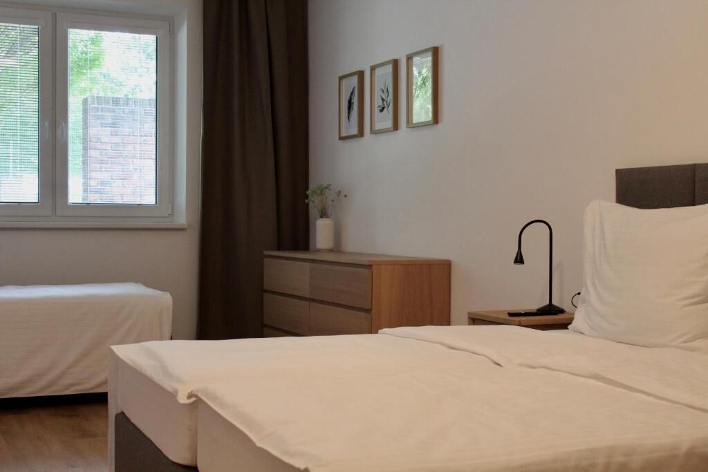 Et soveværelse med to senge, et natbord, en lampe, en kommode og billeder i rammer på væggen.