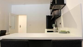 A modern kitchen with a white countertop, black shelving, and a door leading to another room.