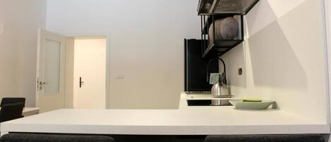 Una cocina moderna con encimera blanca, estanterías negras y una puerta que da a otra habitación.