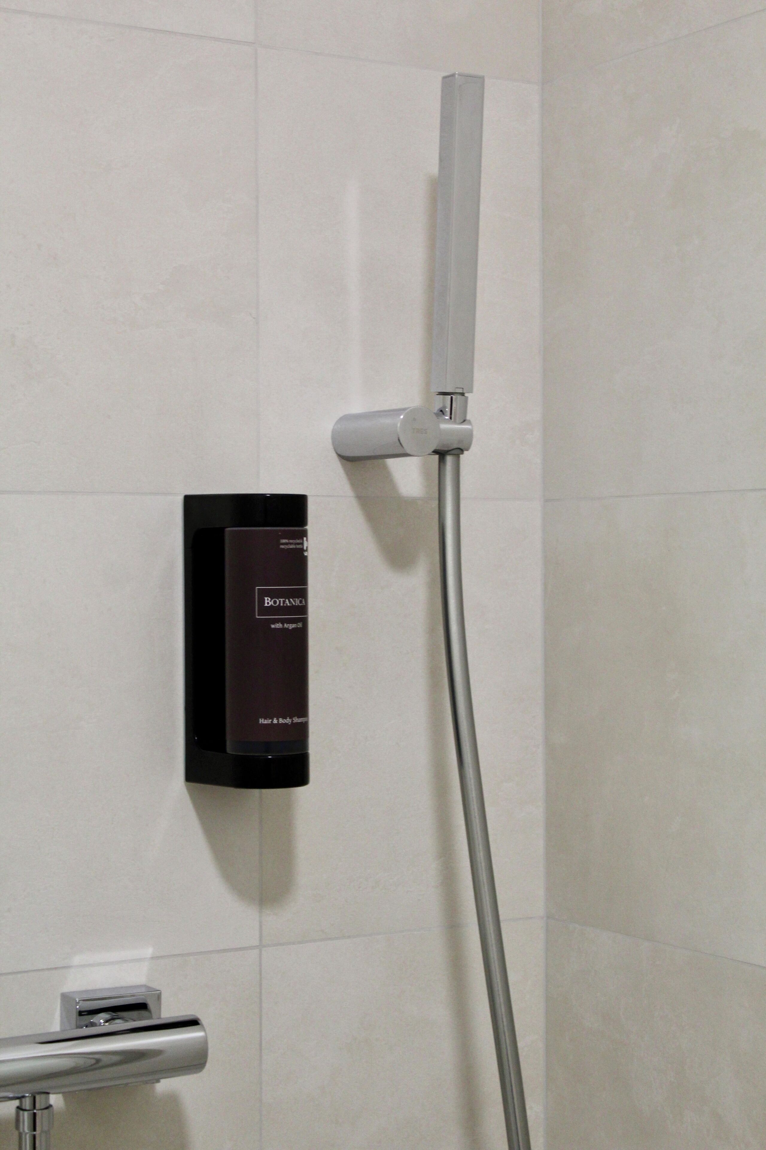 A bathroom with a shower, a wall-mounted hair and body shampoo dispenser, and a towel rack.