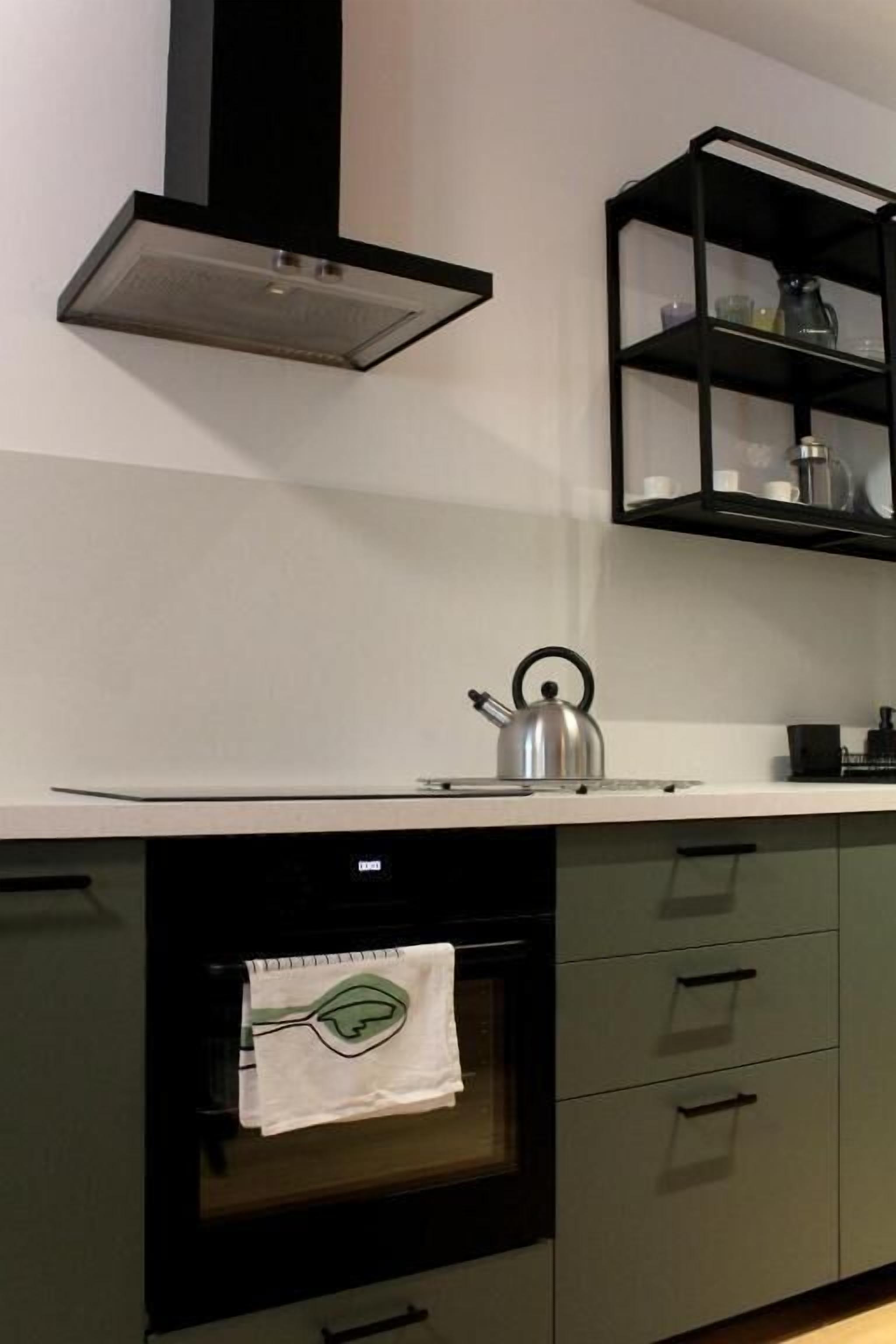 A kitchen with a built-in oven, a kettle, and a shelf with kitchenware.