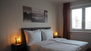 A hotel room with a bed, two bedside lamps, a window with curtains, and a wall with three framed pictures.