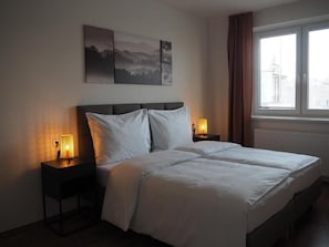 A hotel room with a bed, two bedside lamps, a window with curtains, and a wall with three framed pictures.