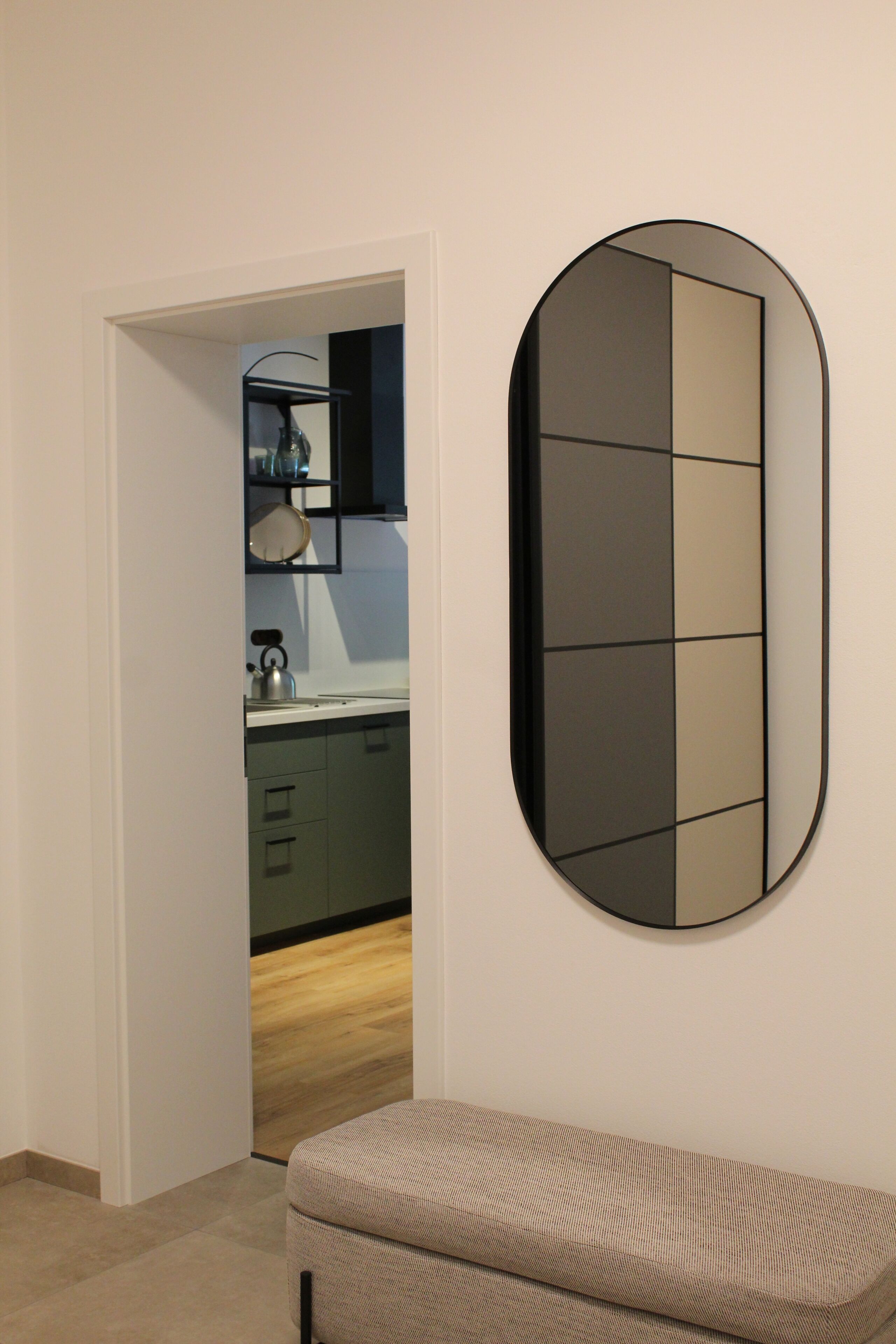 A room with a mirror, a sofa, and a kitchen area in the background.