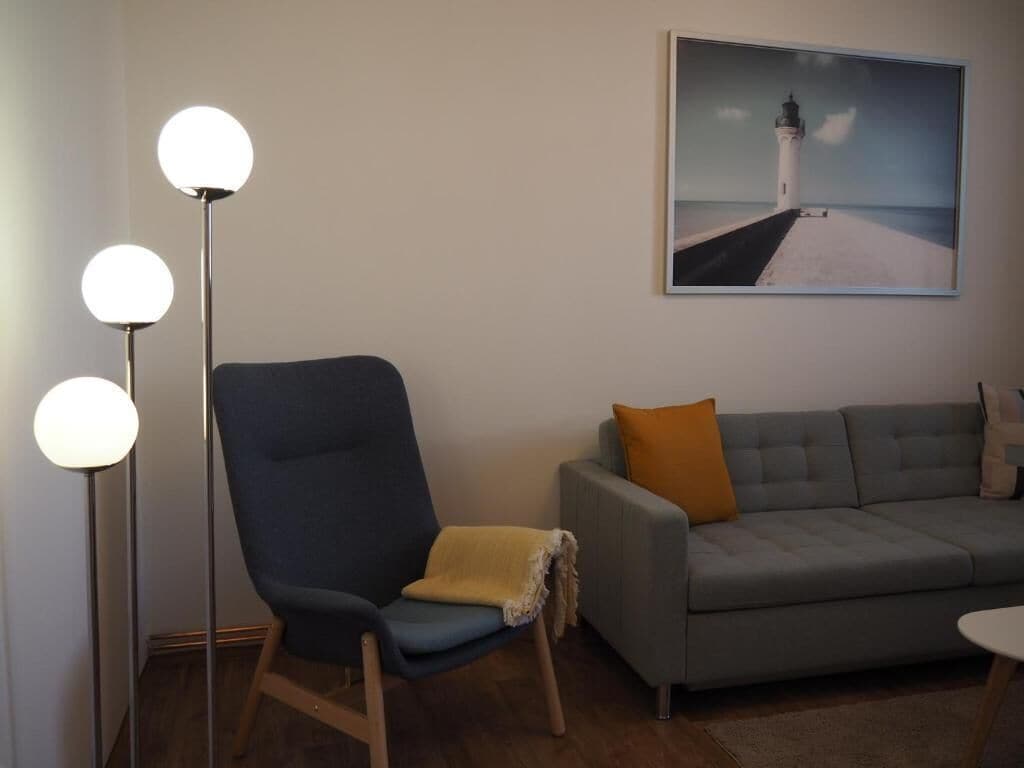 A room with a grey sofa, a blue armchair, and a floor lamp with three spherical lights.