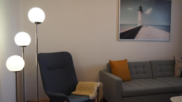 A room with a grey sofa, a blue armchair, and a floor lamp with three spherical lights.