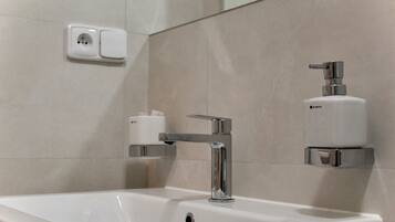 A bathroom with a white sink, chrome faucet, and a soap dispenser mounted on the wall.