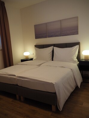 A neatly made bed with white linens, two bedside lamps, a headboard, and a wall-mounted artwork.