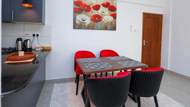 Uma cozinha moderna com área de refeições, incluindo uma mesa com quatro cadeiras, um quadro na parede e uma porta de madeira.