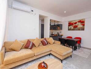 Una sala de estar moderna con un sofá modular, un comedor con sillas rojas y una cocina al fondo.