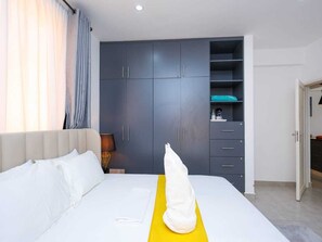 Una habitación de hotel con una cama, un armario y un escritorio pequeño con una lámpara.