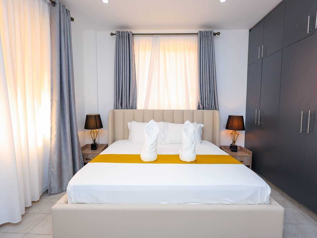 Una habitación de hotel con cama, cortinas, lámparas de noche y un armario.