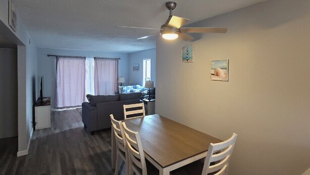 A dining area with a wooden table and chairs, a ceiling fan, and a kitchenette in the background. - Cozy Beach Front Retreat (Pensacola Beach)