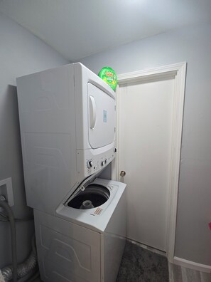 Une petite buanderie équipée d’un lave-linge et d’un sèche-linge superposés, d’une porte et d’une bouche d’aération.