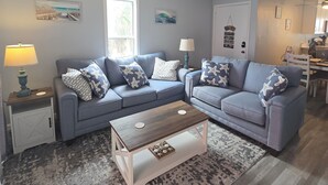 A living room with two sofas, a coffee table, a rug, and a door with a hanging decoration. - Cozy Beach Front Retreat (Pensacola Beach)