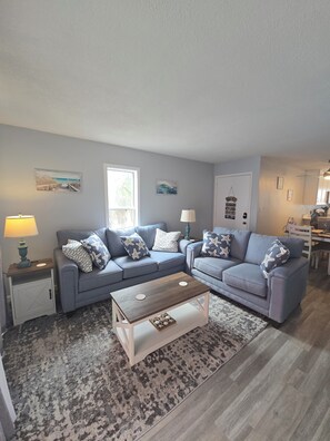 Ein Wohnzimmer mit zwei Sofas, einem Couchtisch, einem Teppich und einer Tür mit einem Wanddekor.