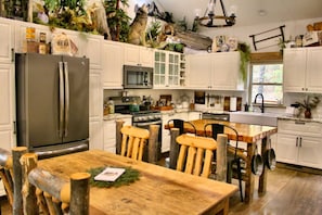 A kitchen with white cabinets, a stainless steel refrigerator, a wooden dining table, and rustic chairs. - Caribou Creek Cabin-Alaska Down South (Hot Springs)