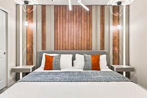 Een moderne slaapkamer met een groot bed, twee nachtkastjes en een wand van houten panelen.