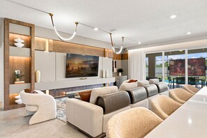A modern living room with a large flat-screen TV, a sofa set, and a dining area with outdoor seating. - Orlando Most Incredible Themed 10br Villa (Clermont)