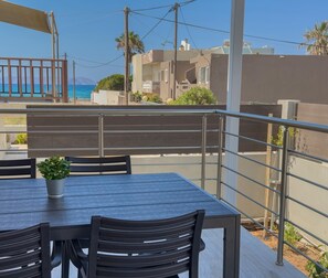 A balcony with a table and chairs, a potted plant, and a view of the sea and buildings. - Eligio Luxury Residence with Private Jacuzzi & Sea View (Gournes Gouvon)