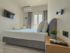 A modern hotel room with a bed, a flat-screen TV, an air conditioning unit, a window with curtains, a potted plant, and a bedside table with a remote control. - Eligio Luxury Residence with Private Jacuzzi & Sea View (Gournes Gouvon)