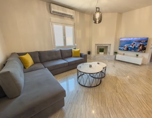 Een moderne woonkamer met een hoekbank, een ronde salontafel, een flatscreen televisie en een open haard.
