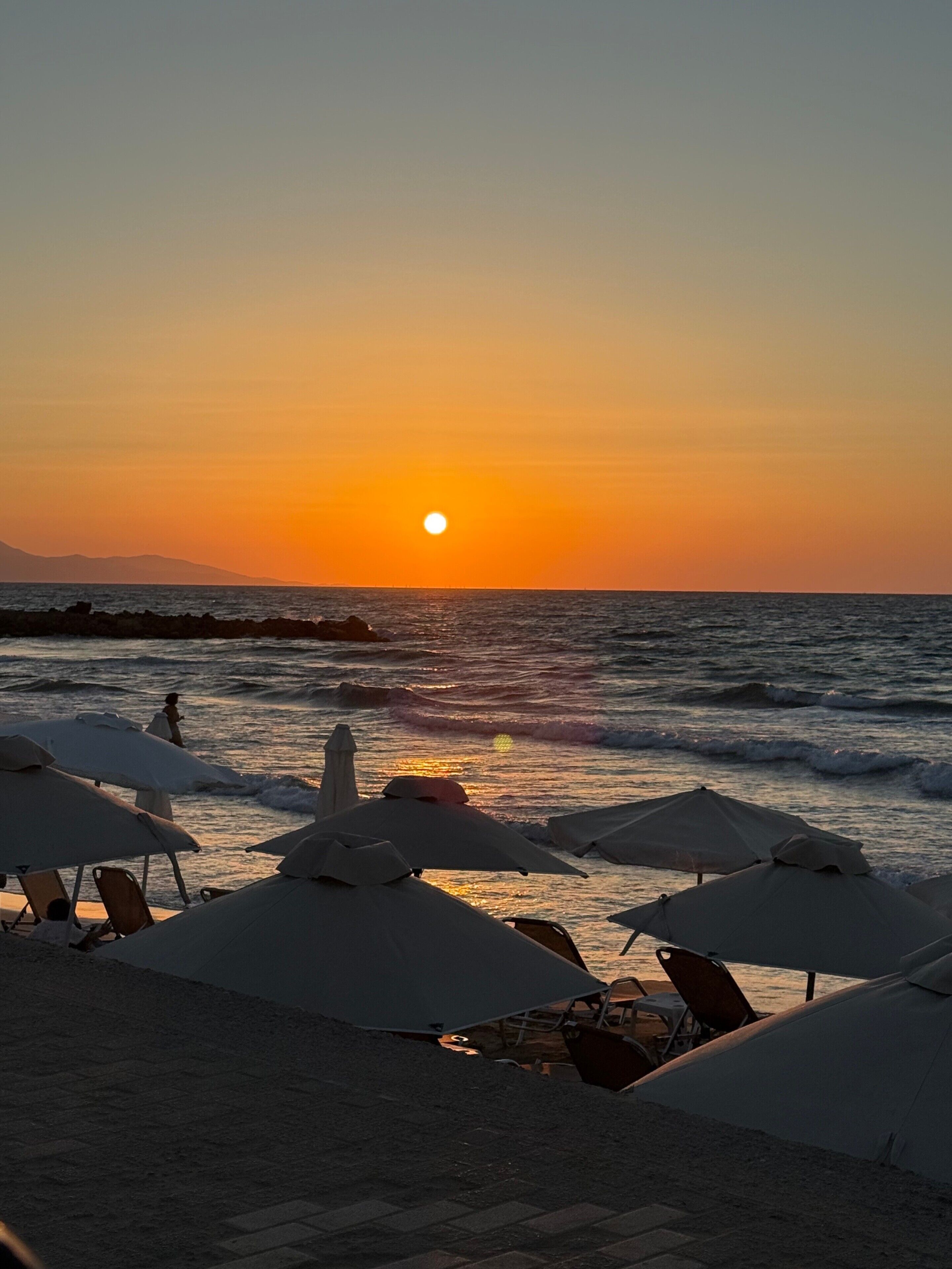 A beach scene with umbrellas and chairs, a sunset, and the ocean.
