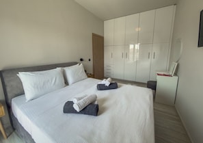 Een slaapkamer met een bed, een kledingkast, een nachtkastje en een spiegel.