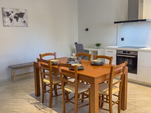 Ein Essbereich mit Holztisch und Stühlen, einer Bank, einer Weltkarte an der Wand und einer Küche mit Herd und Backofen.