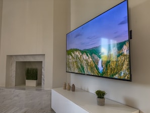 A modern interior with a large flat-screen TV mounted on a white wall, a marble floor, and a minimalist fireplace area. - Eligio Luxury Residence with Private Jacuzzi & Sea View (Gournes Gouvon)
