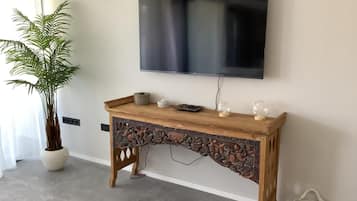 Una consola de madera con intrincados grabados, un televisor de pantalla plana montado encima, una planta en maceta y una cesta tejida en el suelo.