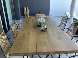 Uma mesa de jantar de madeira com cadeiras trançadas, um banquinho trançado e vasos de vidro com tecido azul.