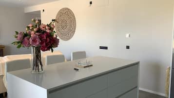 Un moderno comedor con una isla central, sillas blancas, un jarrón de flores y un elemento decorativo en la pared.