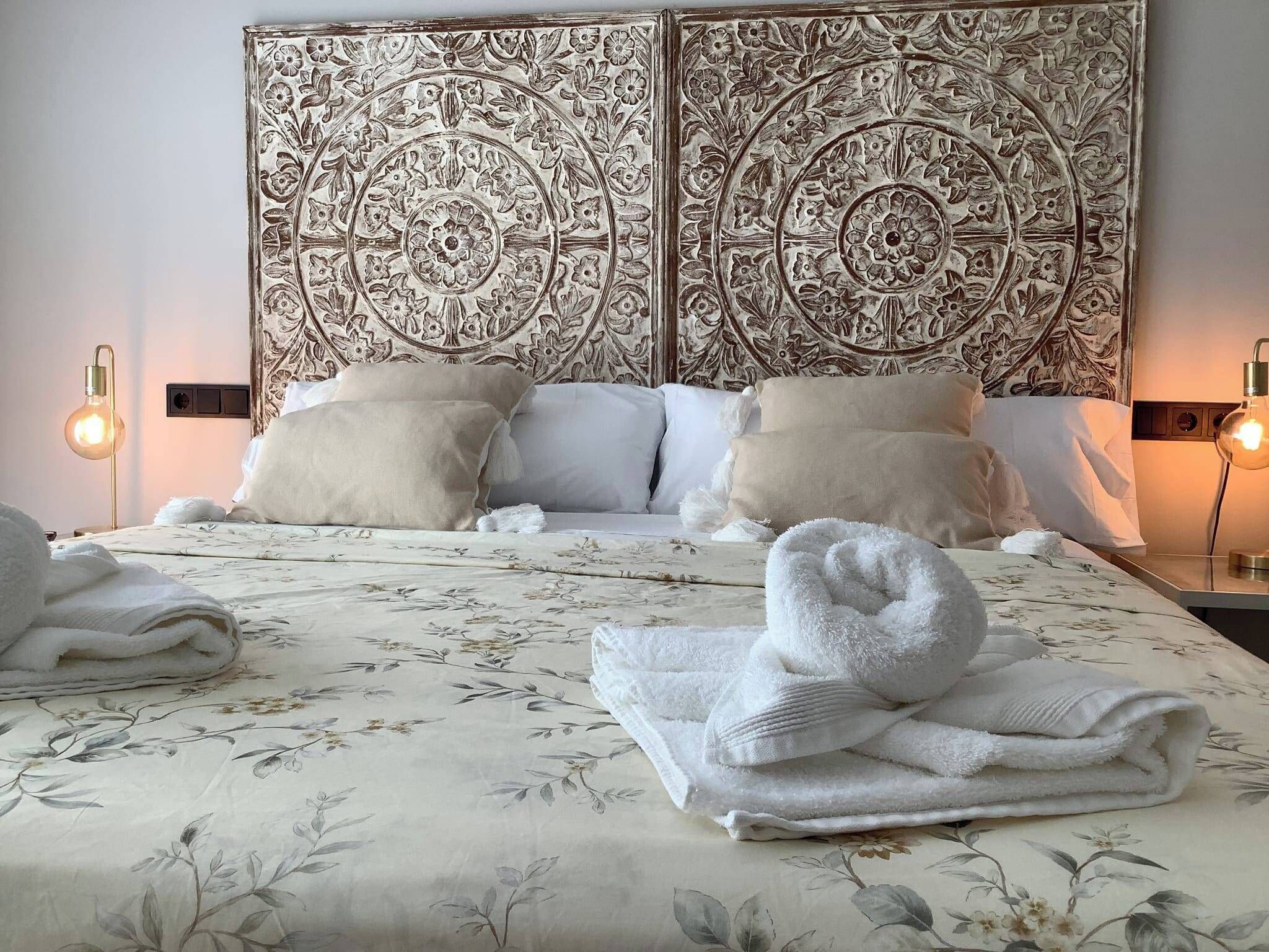 A hotel room with a large bed, floral bedspread, two nightstands with lamps, and a decorative headboard.