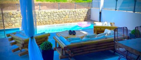 Un área de piscina al aire libre con sillones de madera, una mesa y sillas.