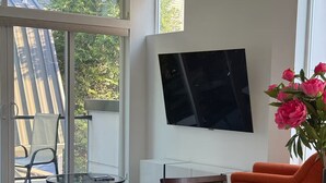 A modern living room with a dining area, large windows, and a flat-screen TV mounted on the wall. - The May Townhome - Full Home (Seattle)