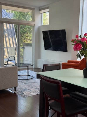 Una sala de estar moderna con comedor, ventanas amplias y un televisor de pantalla plana montado en la pared.