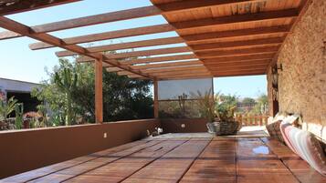 Eine Holzterrasse mit einer Pergola, einem Kakteentopf und einer Bank.