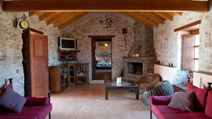 Tunnelmallinen huone, jossa on kiviseinät, puupalkit, takka, televisio, sohva ja kirjahylly.