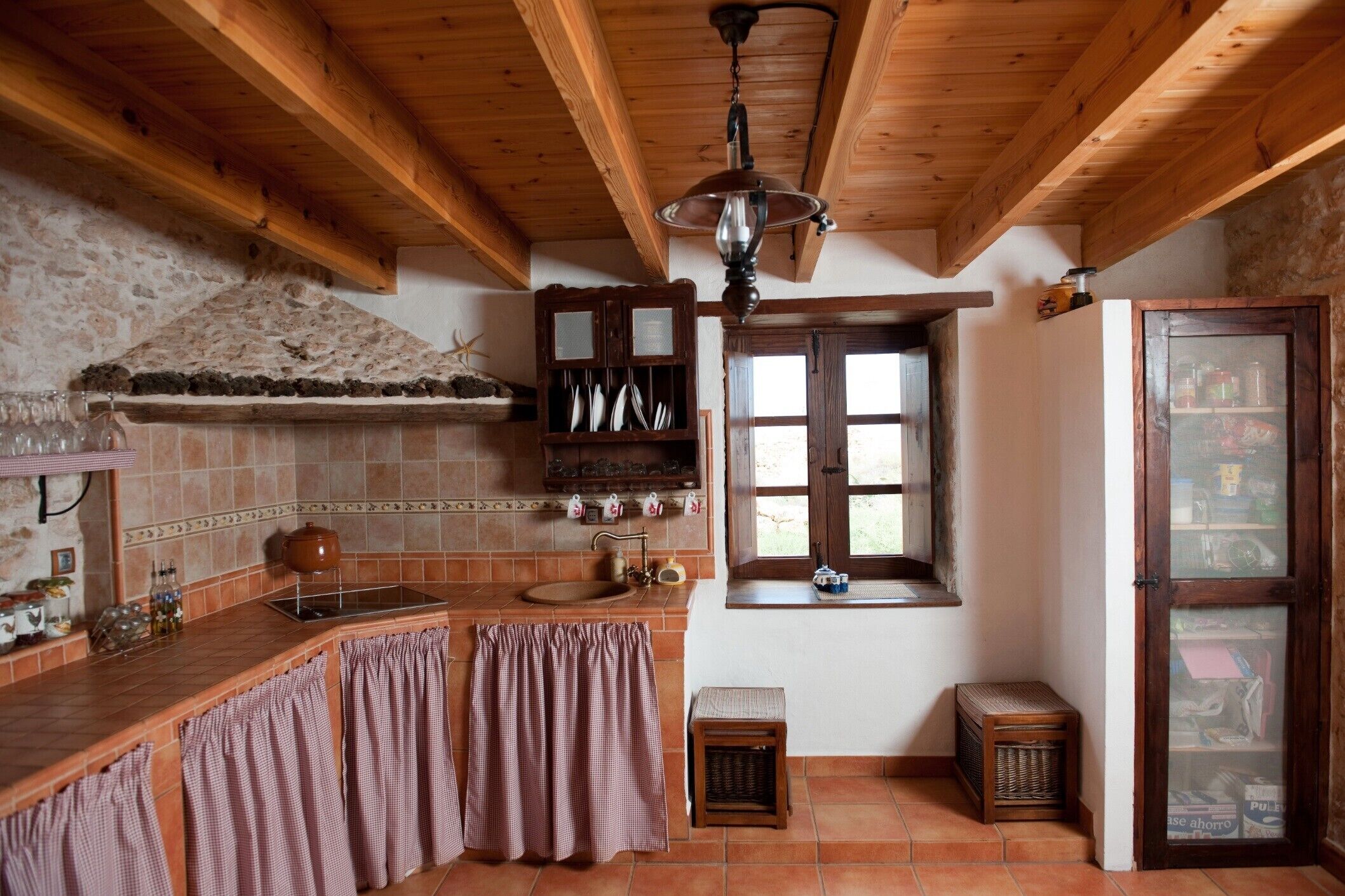 A rustic kitchen with wooden beams, a stone wall, a sink, a window, and a cabinet.