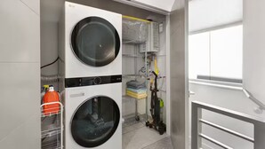 A laundry room with two stacked washers and dryers, a drying rack, and a utility cart with cleaning supplies. - Bright & Cozy Seward Park 1BR w/Rooftop Patio + AC (Seattle)