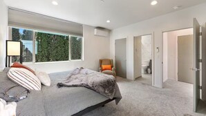 A modern bedroom with a large bed, a chair, and a view of a bathroom through an open door. - Bright & Cozy Seward Park 1BR w/Rooftop Patio + AC (Seattle)