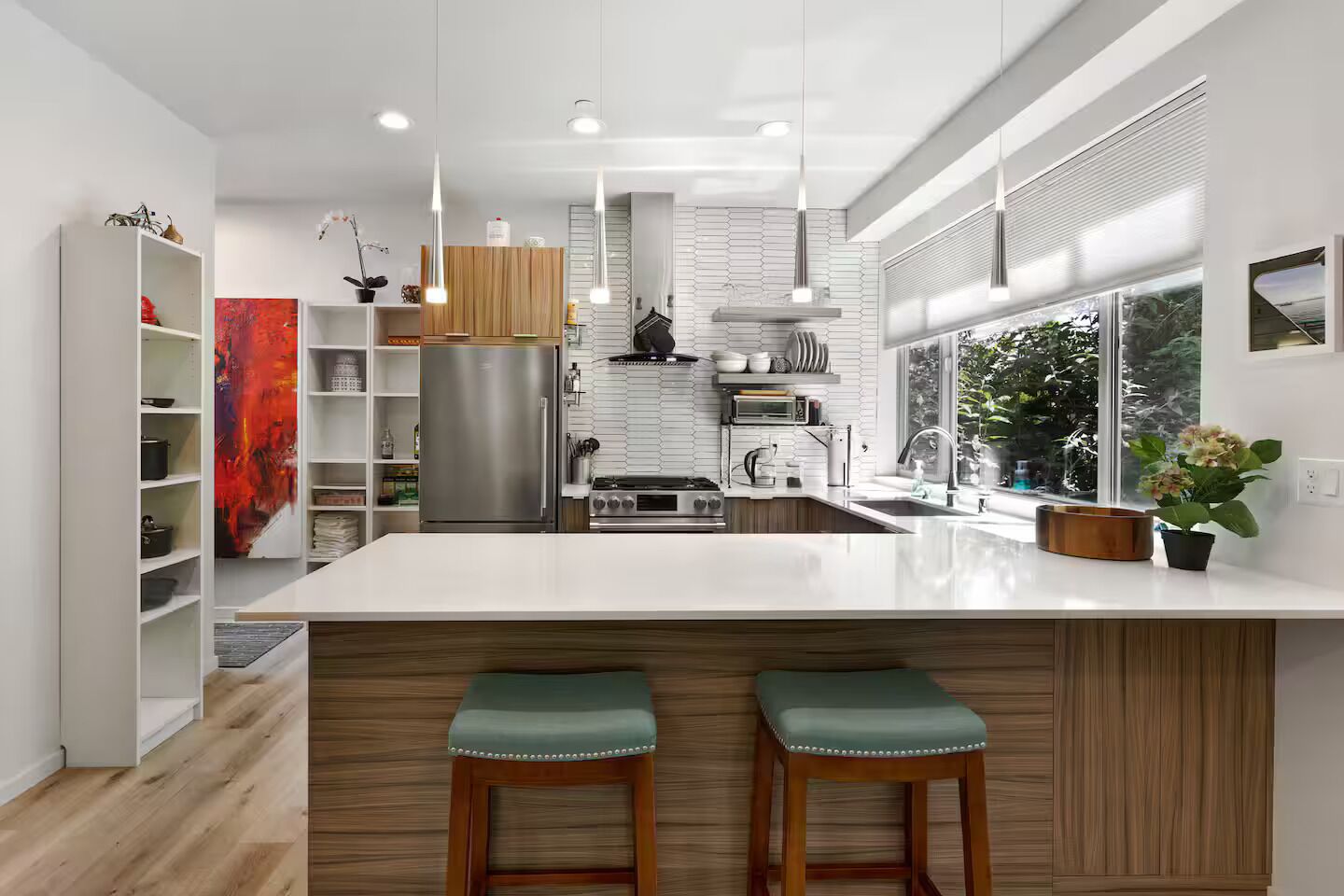 A modern kitchen with a large island, stainless steel appliances, and a view of greenery outside.