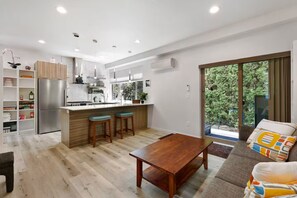 A modern kitchen with a built-in island, bar stools, and a dining table. - Bright & Cozy Seward Park 1BR w/Rooftop Patio + AC (Seattle)