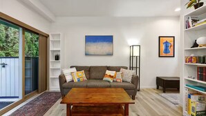 A modern living room with a grey sofa, wooden coffee table, and a bookshelf. - Bright & Cozy Seward Park 1BR w/Rooftop Patio + AC (Seattle)