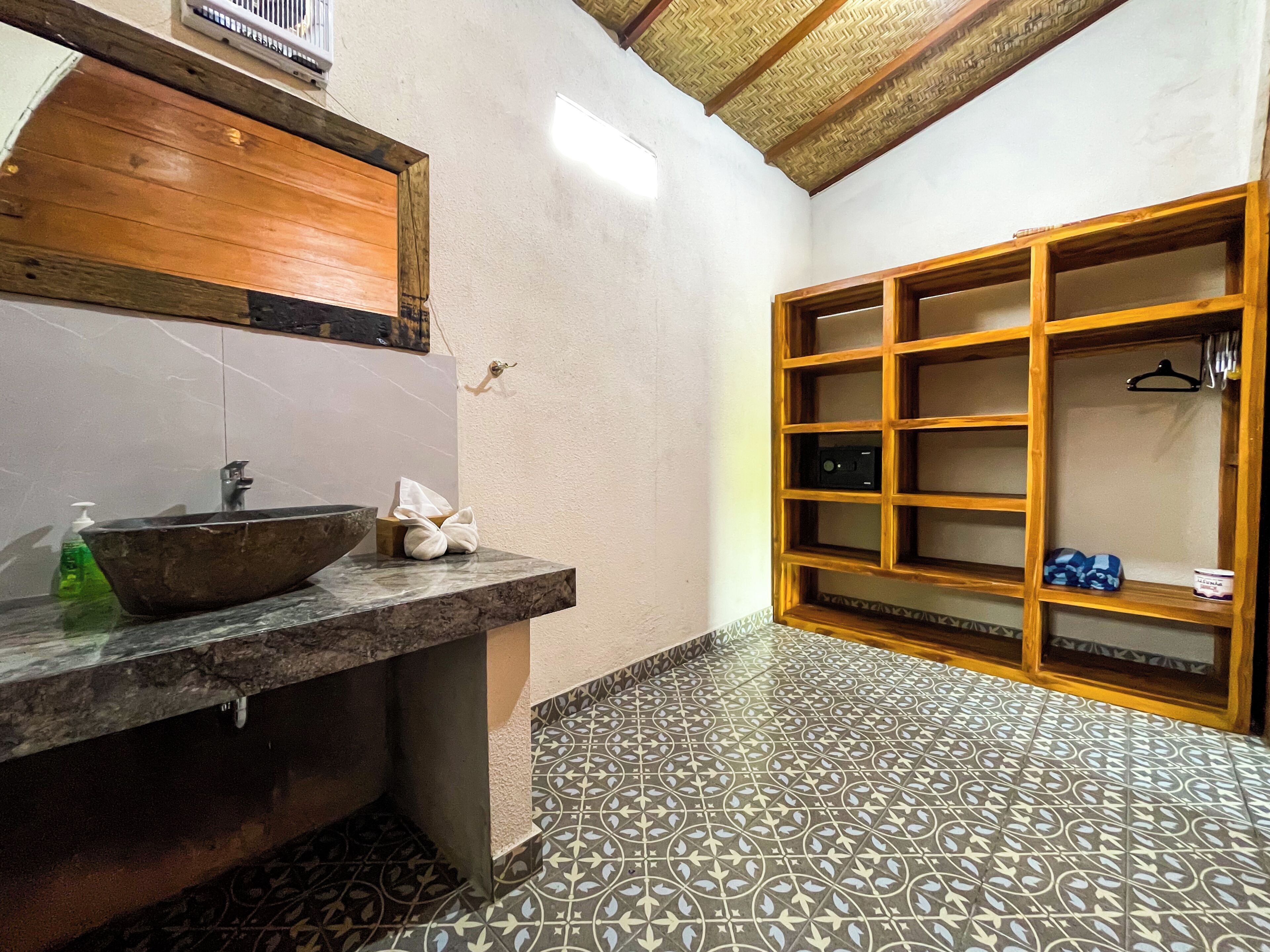 A bathroom with a wooden vanity, a large basin sink, a towel dispenser, and a tiled floor.