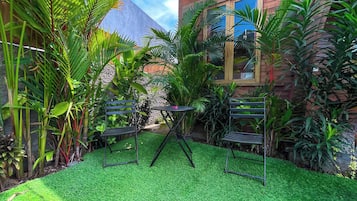 A garden with artificial grass, two metal chairs, and a table.