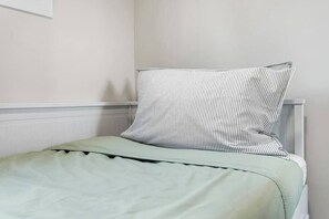 Ein Einzelbett mit einer grünen Bettdecke und einem Kissen in Schwarz und Weiß gestreift.