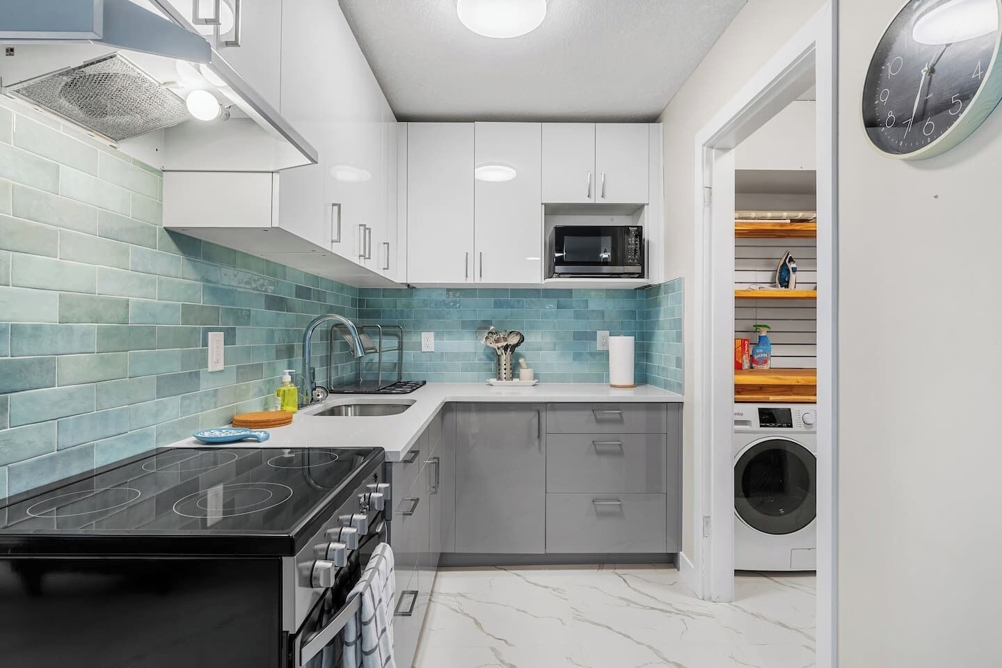 A compact kitchen with a stove, sink, microwave, and a washing machine in the corner.